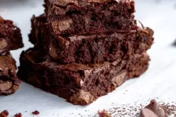 Brownies squares cut and stacked on top of each other. With a few chocolate chips laying next to them.