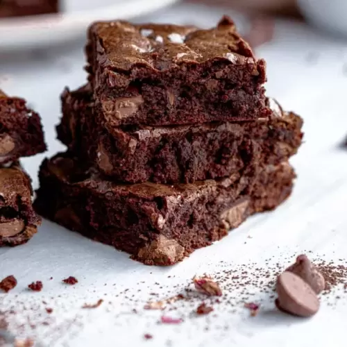 Brownies squares cut and stacked on top of each other. With a few chocolate chips laying next to them.