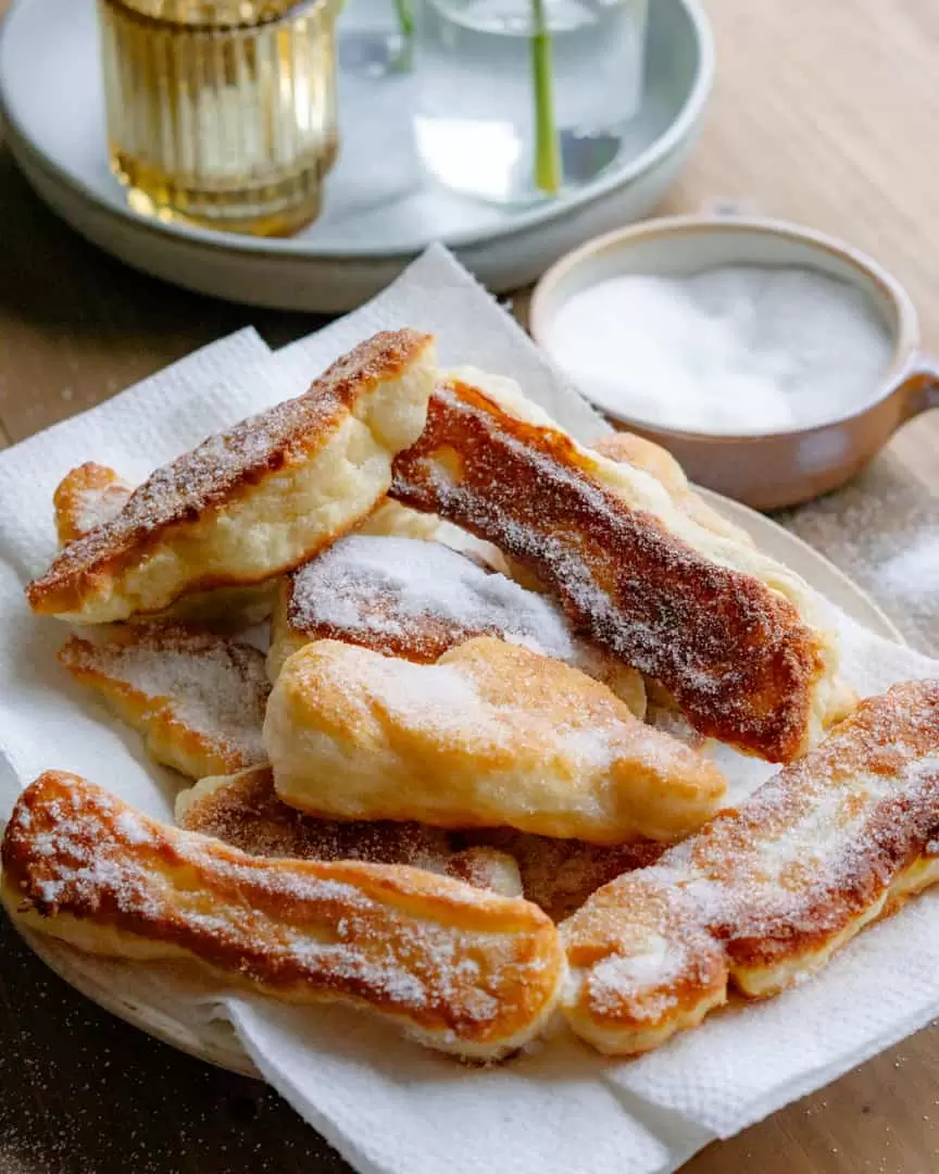 Zeppole on a plate with a bowl of sugar nearby.