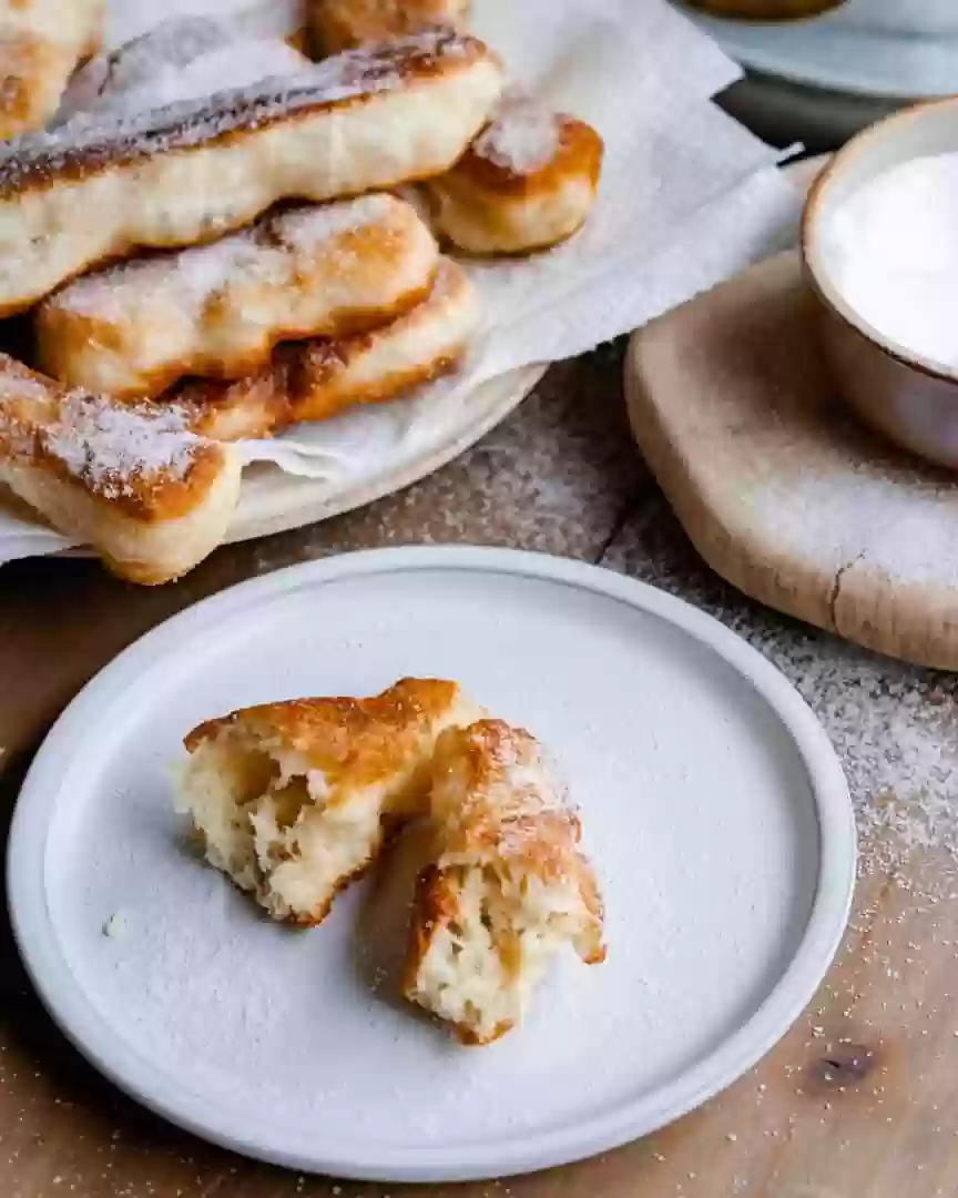 Zeppole on a plate broken in half with a plate of zeppole behind it.