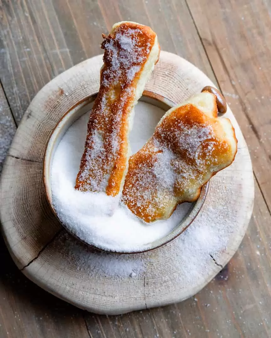 Two zeppole dipped in a bowl of sugar