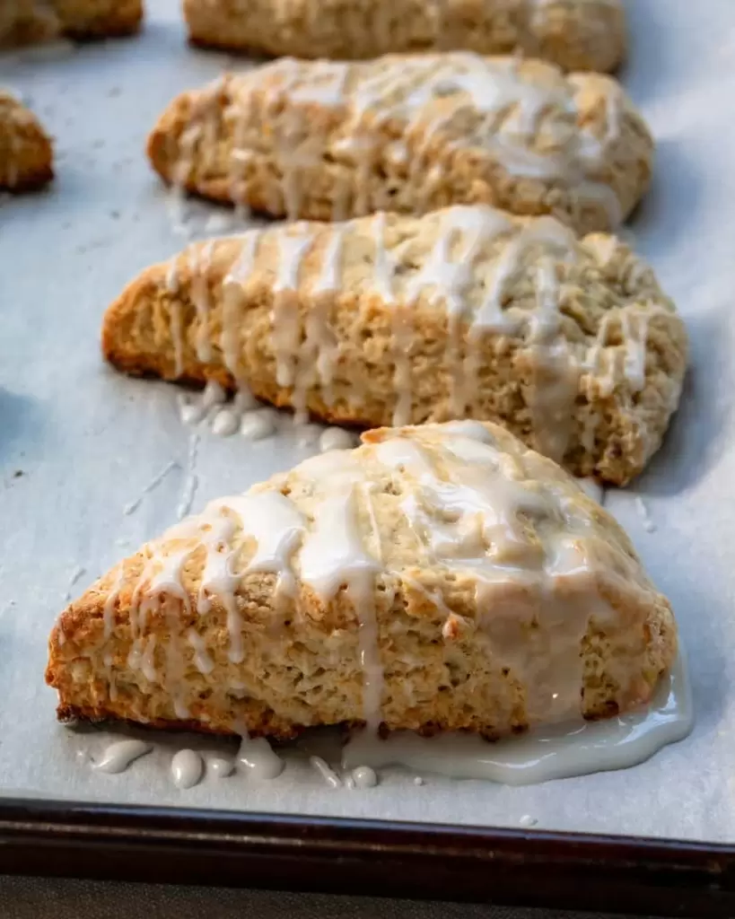 Scones with a sugar drizzle on top are lined up on a baking tray.