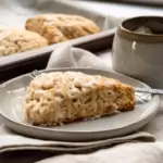 A scone on a plate with a cup of tea next to it.