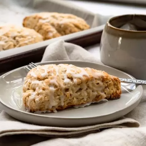 A scone on a plate with a cup of tea next to it.