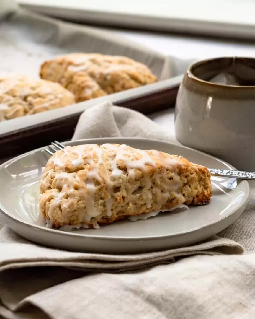 A scone on a plate with a cup of tea next to it.