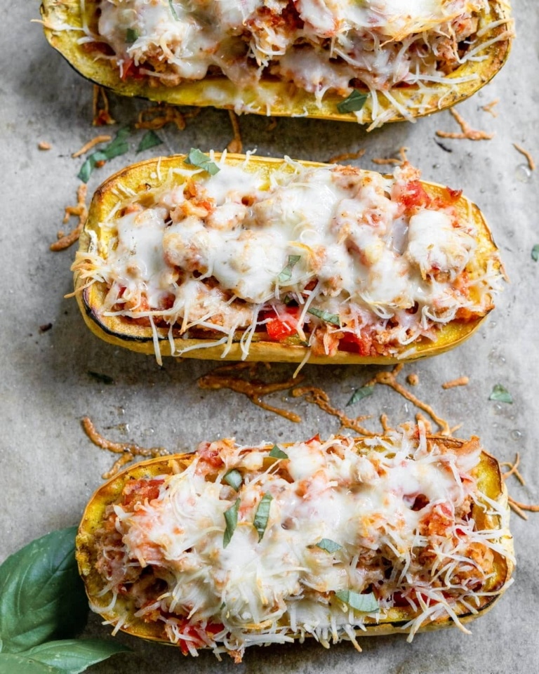 Delicata Squash cut in half on a baking sheet. It has been stuffed with veggies and ground beef and topped with melted mozzarella cheese.