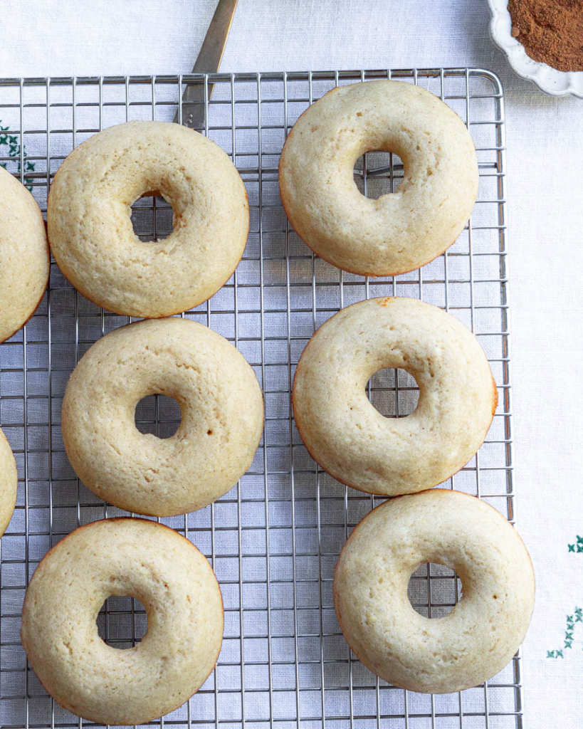 Baked and unfrosted donuts on a cooling rack.