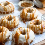 Donuts on a cutting board, the donuts have a vanilla glaze with a caramel sauce drizzle.