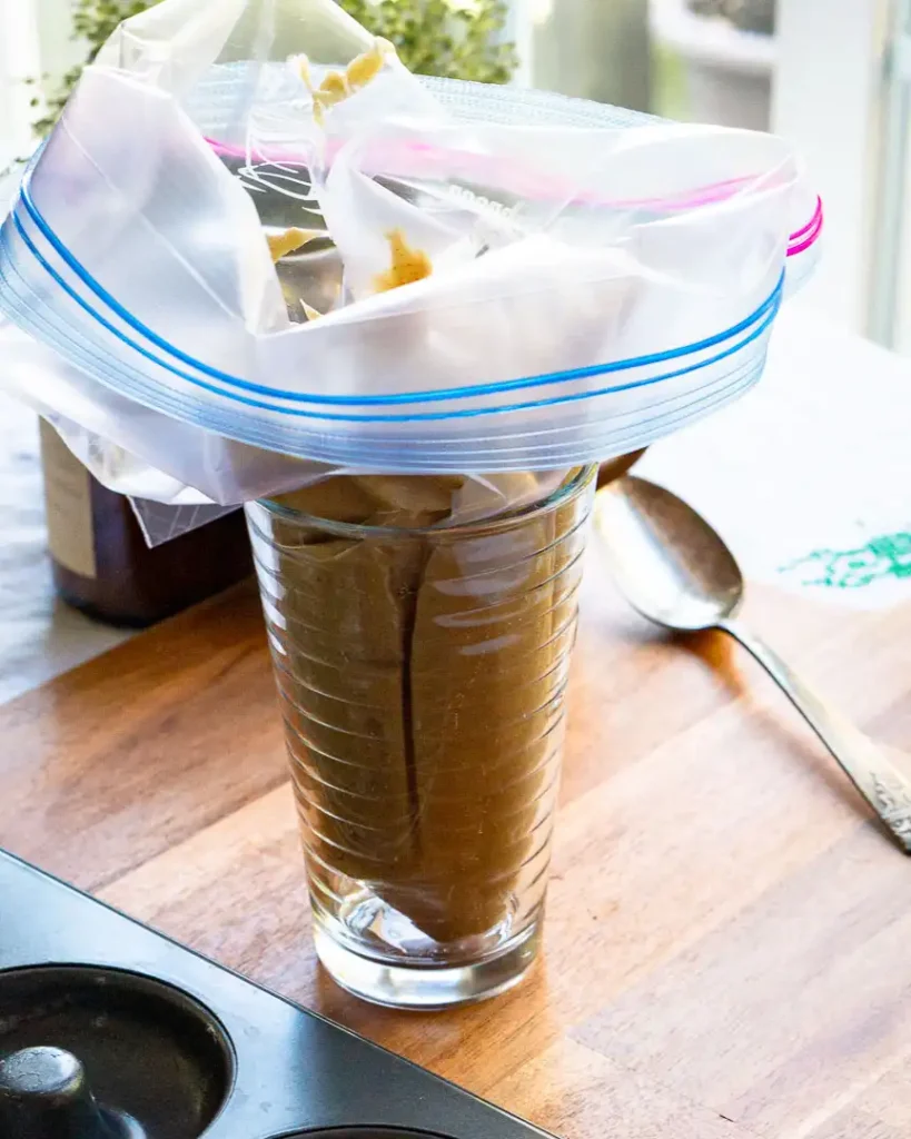 A tall glass jar with a ziplock bag in it. The bag is filled with donut batter.