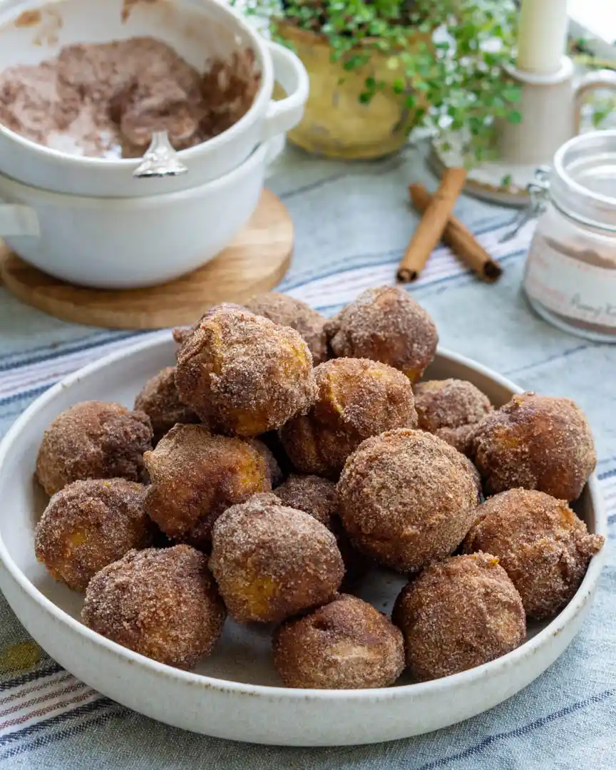 Pumpkin donut holes coated in cinnamon sugar and piled onto a plate.