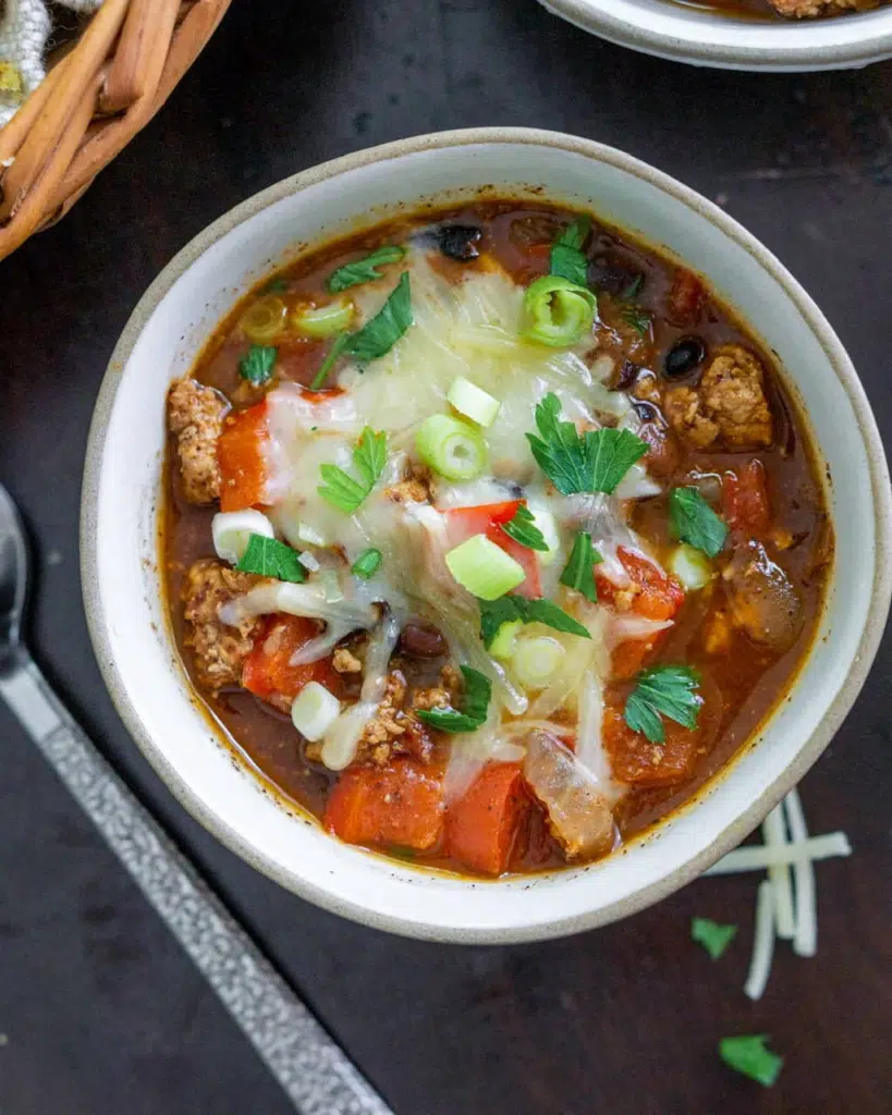 Bowl of turkey chili with shredded cheese, green onions , and fresh parsley sprinkled on top.