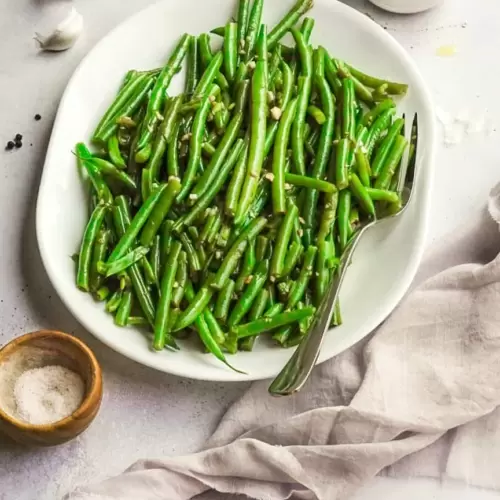 Platter of cooked green beans with olive oil pitcher, salt and napkin next to serving dish.