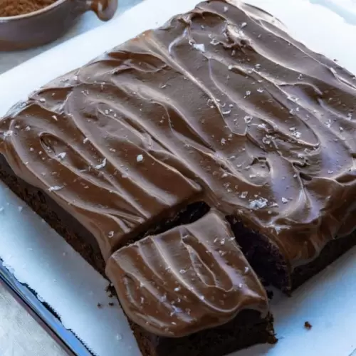 One layer chocolate cake that is in a square shape with one piece cut and slightly pulled away from the rest of the cake. The top the cake is frosted with chocolate frosting and sprinkled with large sea salt flakes.