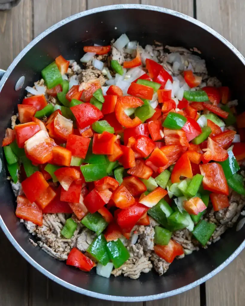 A pot of cooked ground turkey with chopped raw red and green peppers, and raw chopped onions on top.