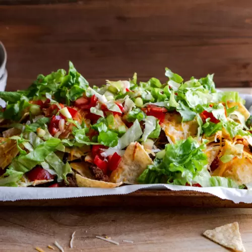 Nachos on a baking sheet loaded with fresh veggies like lettuce, tomatoes, avocados.