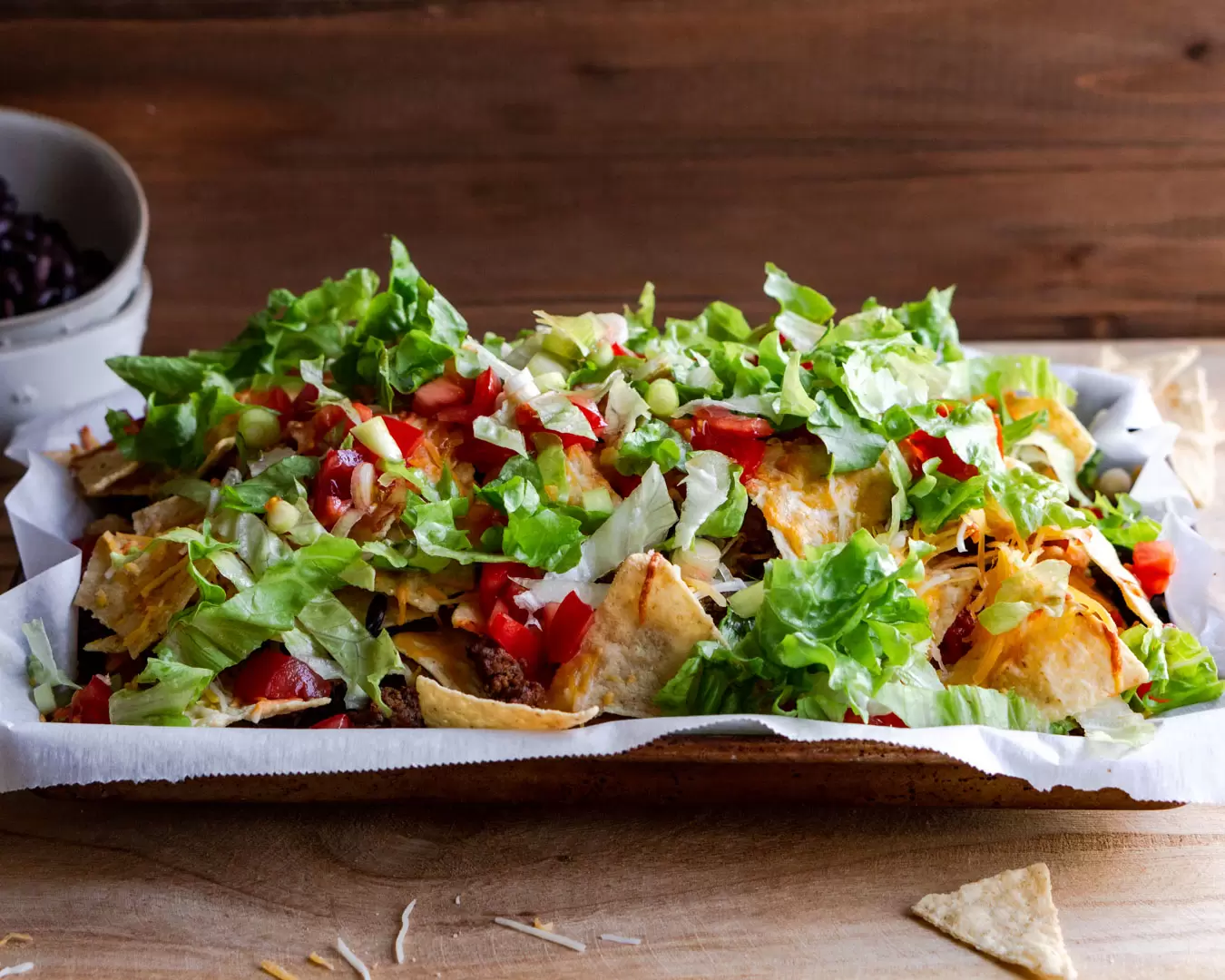 Nachos on a baking sheet loaded with fresh veggies like lettuce, tomatoes, avocados.