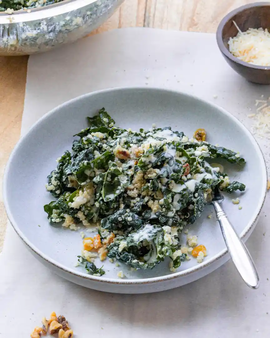 plate of kale and quinoa salad with fork and small bowl of shredded cheese