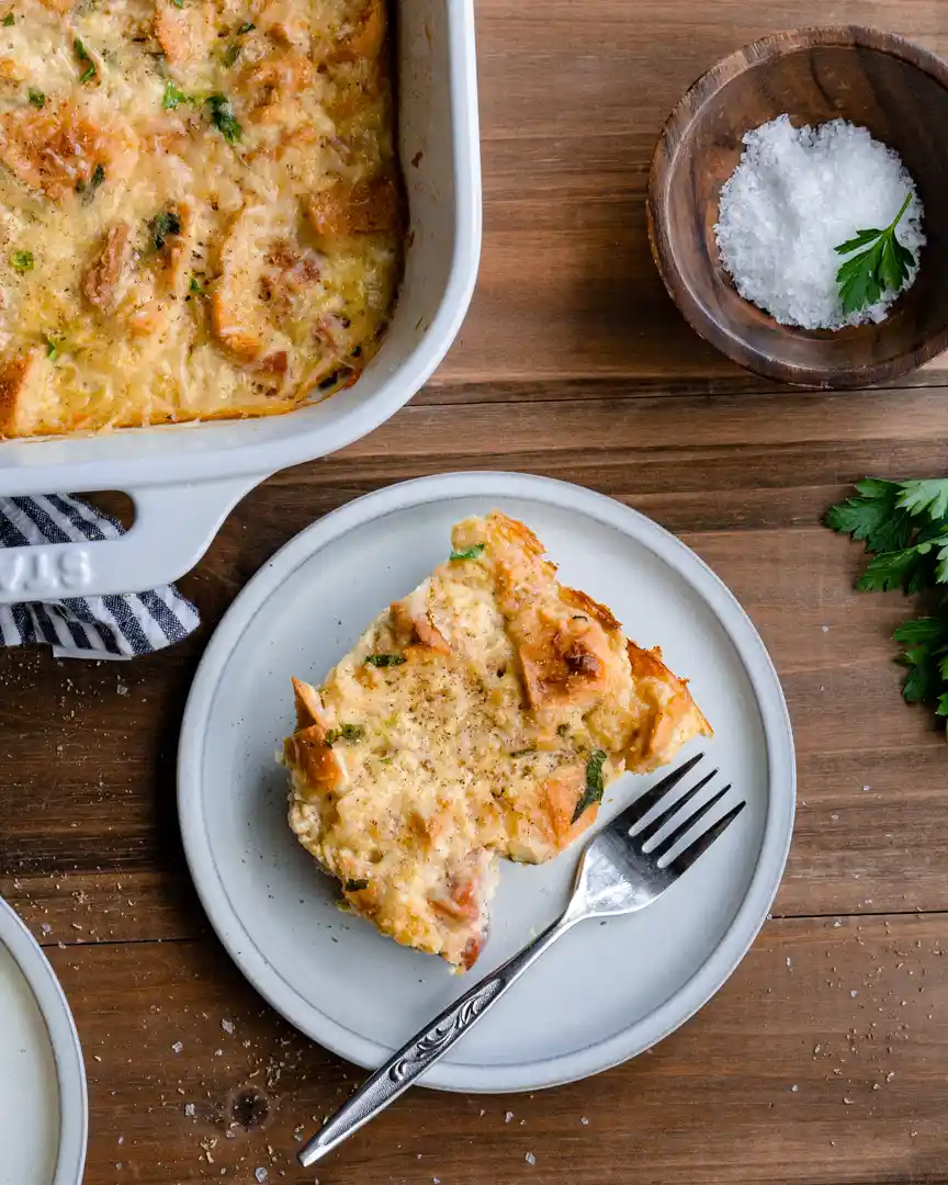 a cut square of ham and cheese strata on a plate with a fork