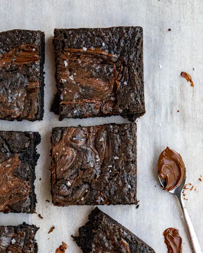 cut Nutella brownies squares next to a spoon filled with Nutella