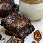 One bowl Nutella Brownies stacked on top of each other next to a mug and a small spoon filled with nutella