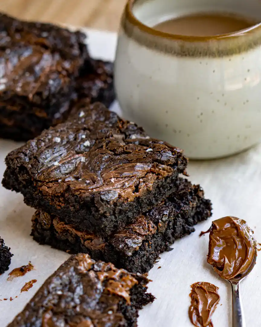 One bowl Nutella Brownies stacked on top of each other next to a mug and a small spoon filled with nutella