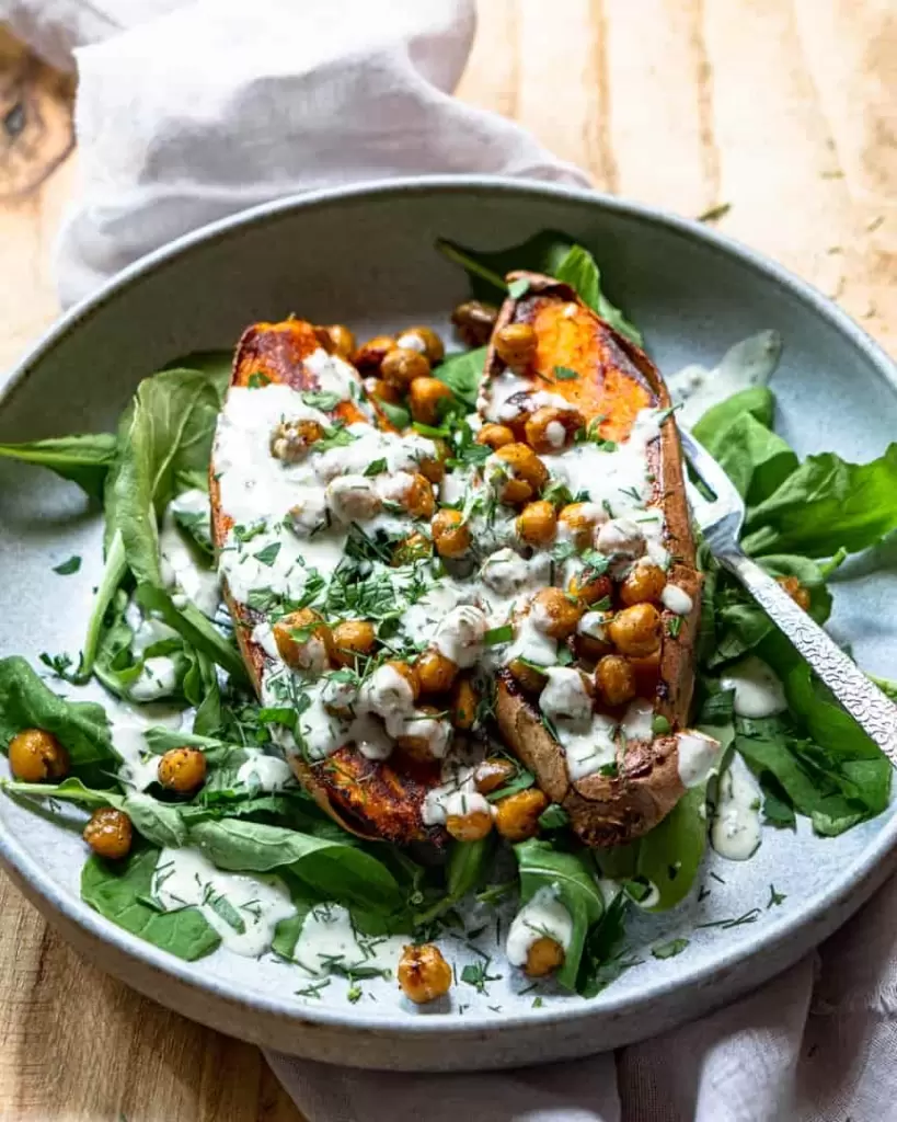 roasted sweet potato and chickpeas in a bowl topped with dressing and herbs