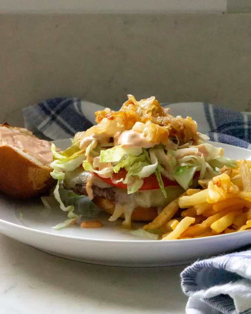 A burger with toppings on a plate with the top of the bun to the side and french fries next to it.