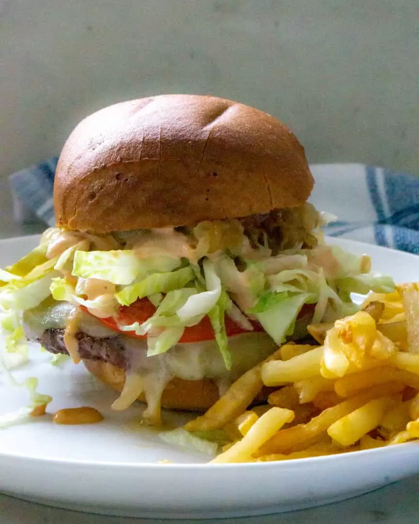 Hamburger with a bun and toppings with a side of fries on a plate