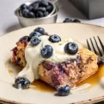 Blueberry baked oatmeal slice with yogurt, maple syrup and fresh blueberries on top.