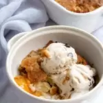 small round bowl with peach cobbler topped with two scoops of ice cream