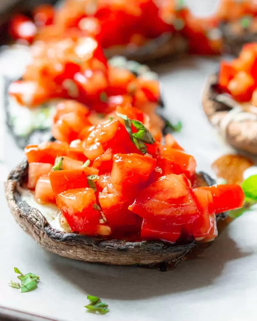 Portobello mushrooms with tomato bruschetta on top of them.