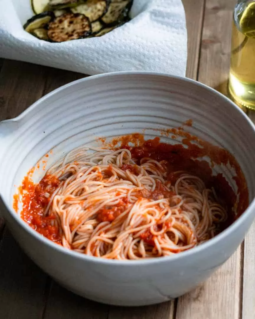 A large bowl of spaghetti with a smaller bowl of fried zucchini on paper towels next to it.