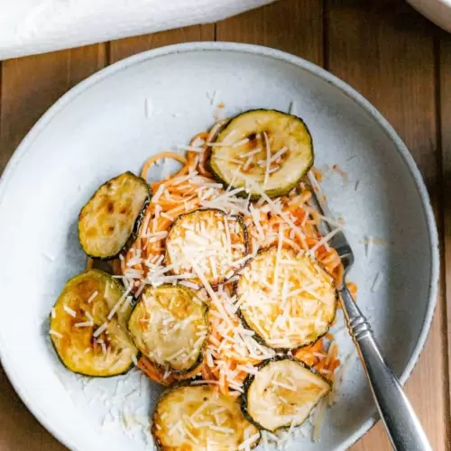 A plate of spaghetti with fried zucchini rounds and sprinkled with shredded parmesan cheese.