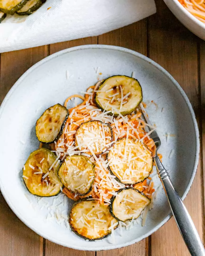 A plate of spaghetti with fried zucchini rounds and sprinkled with shredded parmesan cheese.