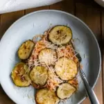 A plate of spaghetti with fried zucchini rounds on top of the spaghetti. Shredded parmesan cheese sprinkled over the dish.