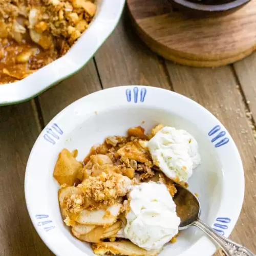 Apple Crips in a bowl with two scoops of ice cream and a spoon