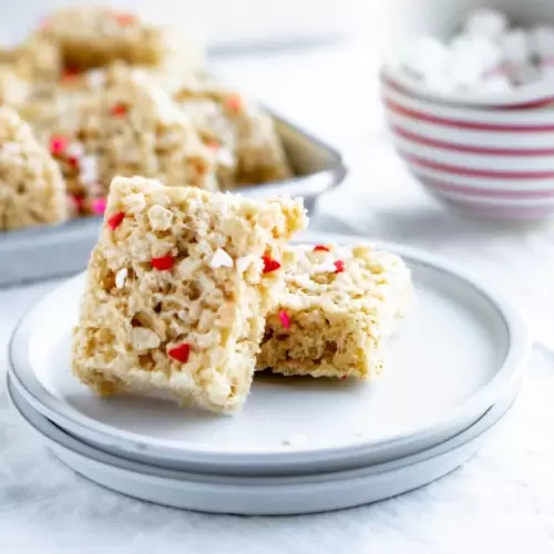 Two rice krispie squares stacked on a plate with a pile of rice krispie treats behind them on a platter