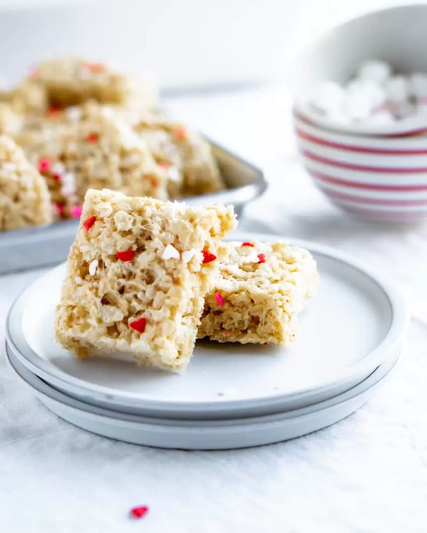 Two rice krispie squares stacked on a plate with a pile of rice krispie treats behind them on a platter