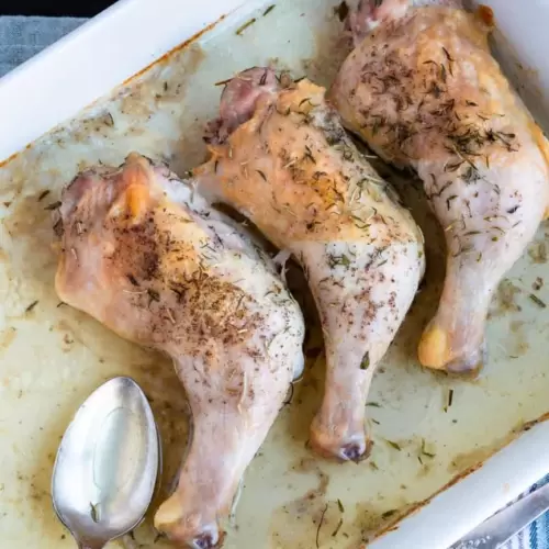 Three baked chicken quarters laying next to each other in a baking pan with a spoon for pan juices.