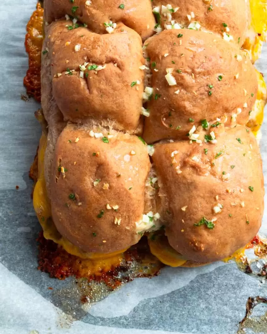 Top down view of slider buns covered in minced garlic, parsley, and melted butter.