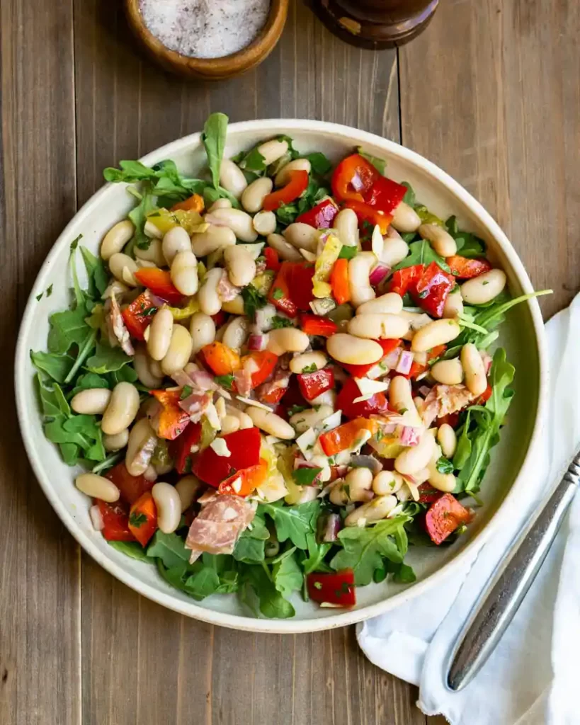 Italian grinder salad with beans, red peppers, salami on a bed of arugula.