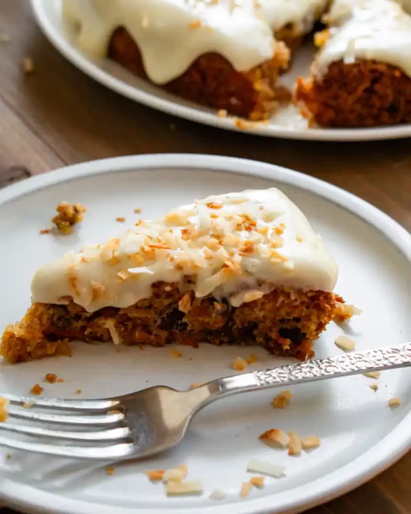 A slice of frosted carrot cake on small plate with a fork.