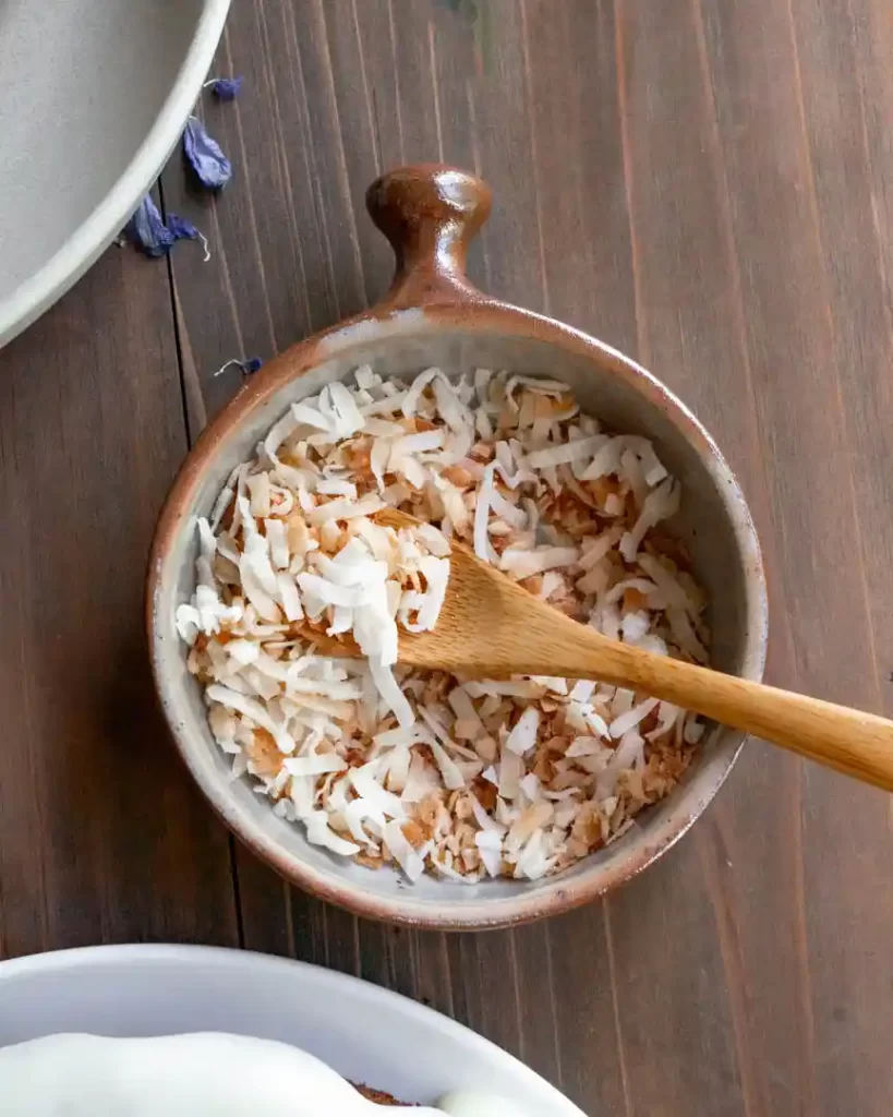 A small bowl of toasted coconut flakes with a spoon in the bowl.