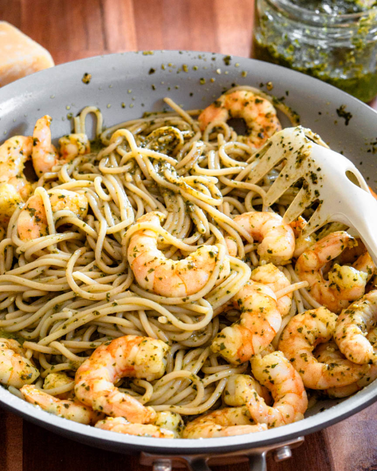 Spaghetti with pesto and shrimp in a sauté pan with a spaghetti fork laying in the pan.