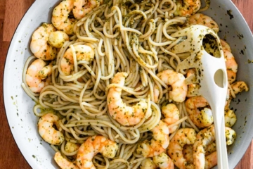 A large sauté pan with spaghetti tossed in basil pesto and topped with shrimp.