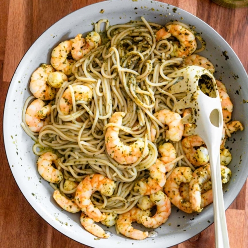 A large sauté pan with spaghetti tossed in basil pesto and topped with shrimp.