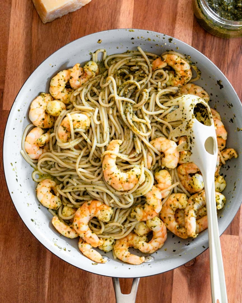 A large sauté pan with spaghetti tossed in basil pesto and topped with shrimp.