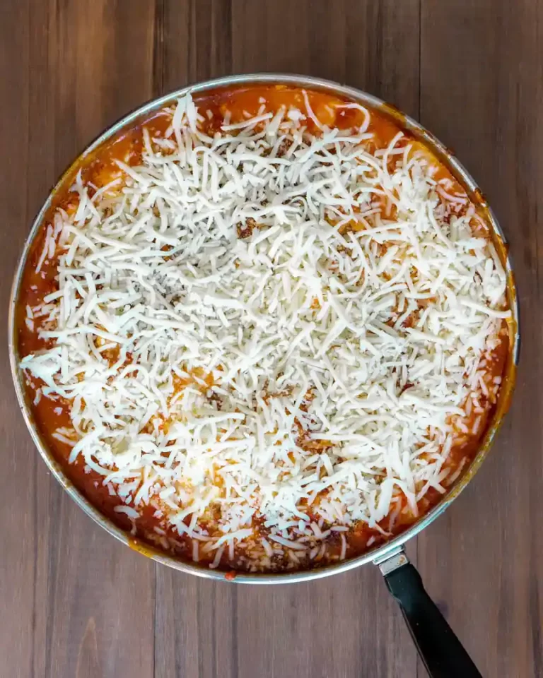 Shredded mozzarella cheese on top of lasagna that's being made in a skillet.