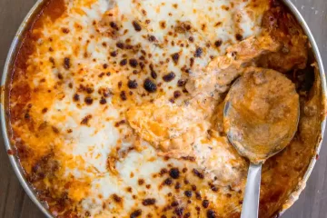 A skillet pan of lasagna with mozzarella that has been broiled. There is a scoop taken out of the pan and a spoon resting in it's place.