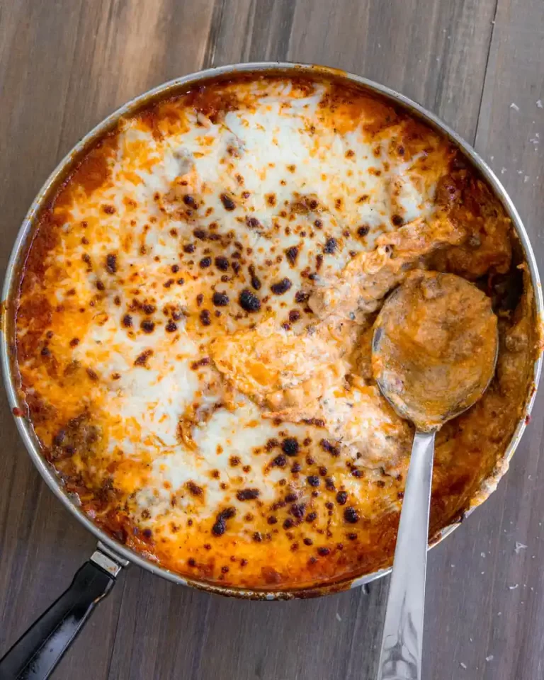 A skillet pan of lasagna with mozzarella that has been broiled. There is a scoop taken out of the pan and a spoon resting in it's place.